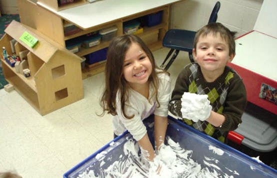 Two children playing with shaving cream in a blue bin