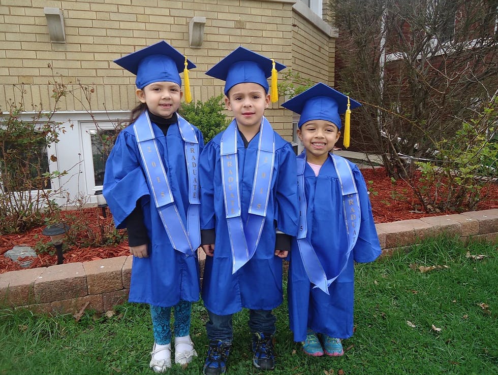 Three children in blue graduation caps and gowns standing outdoors