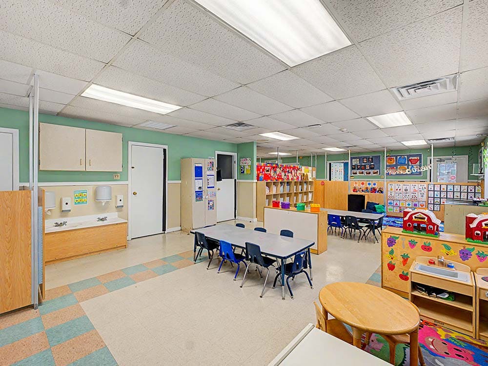 An empty childcare classroom with small tables, chairs, and play areas