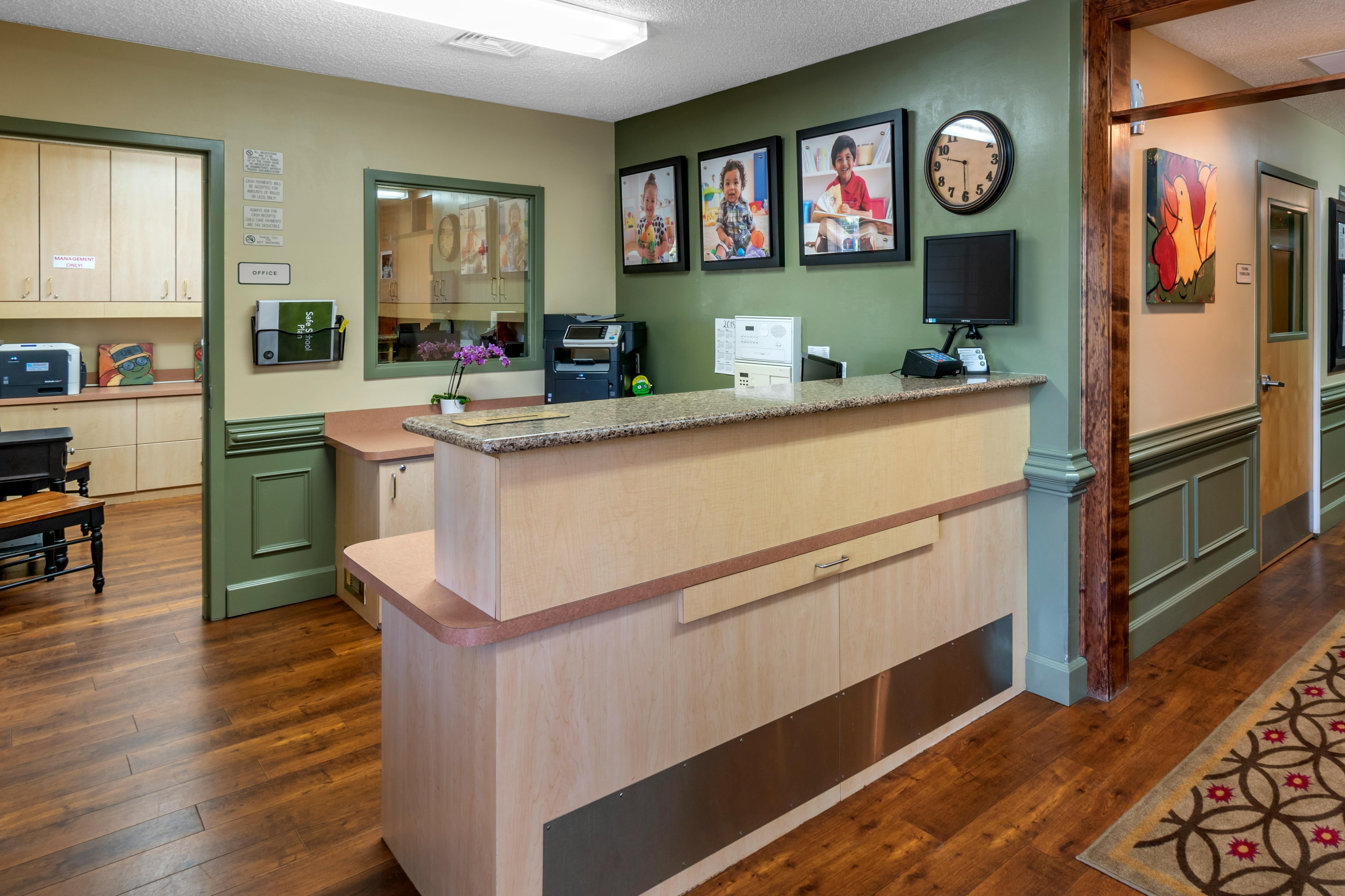 Reception desk with three framed photos of children and a wall clock