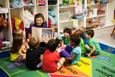 Adult reading a book to a group of children in a classroom