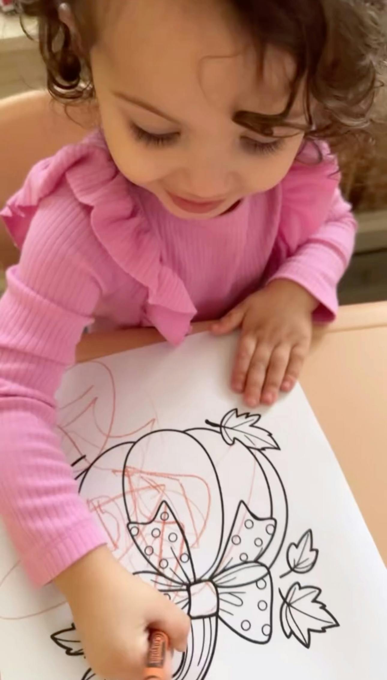 Child coloring a pumpkin drawing with a crayon