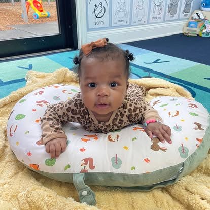 Child in leopard print onesie doing tummy time on a patterned pillow