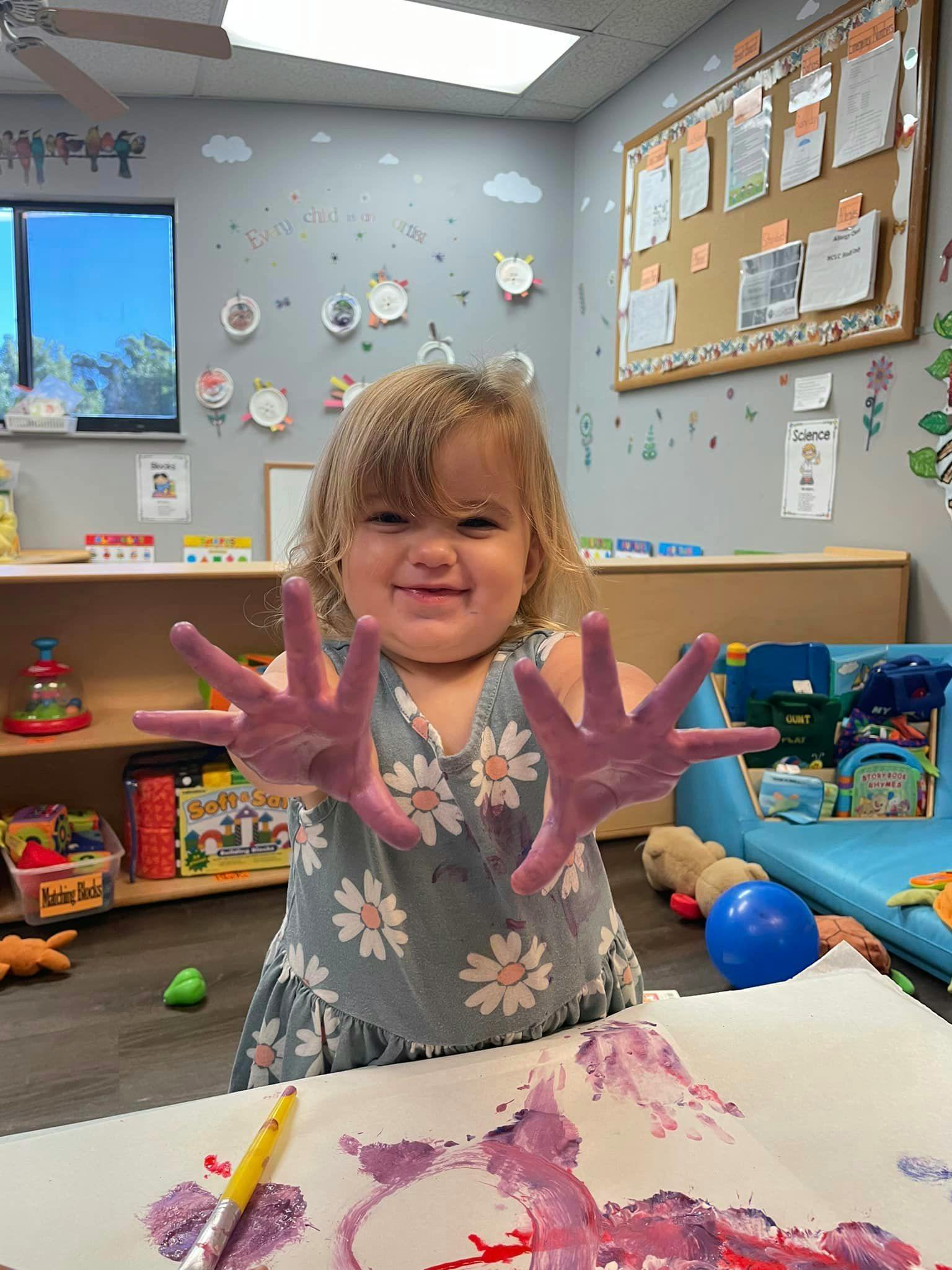 Child with purple paint on hands in a classroom