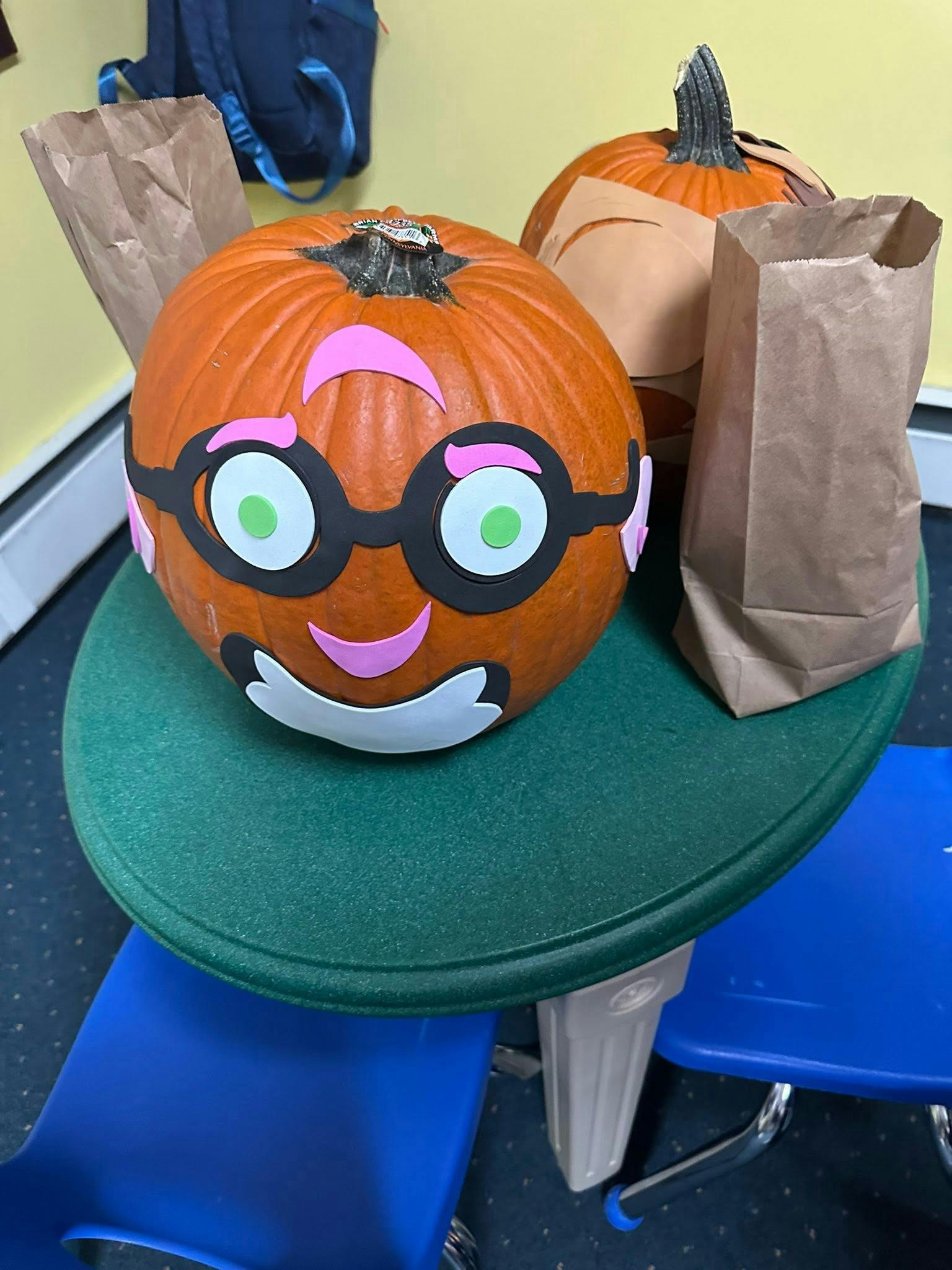 Pumpkin decorated with a cartoon face and glasses on a small green table