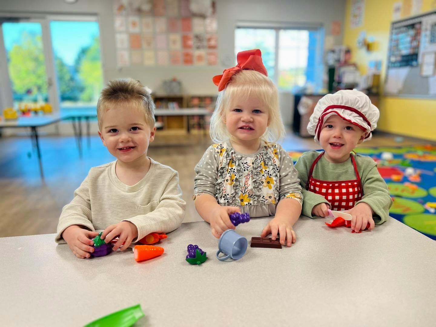 Three children playing with toys at a table in a classroom