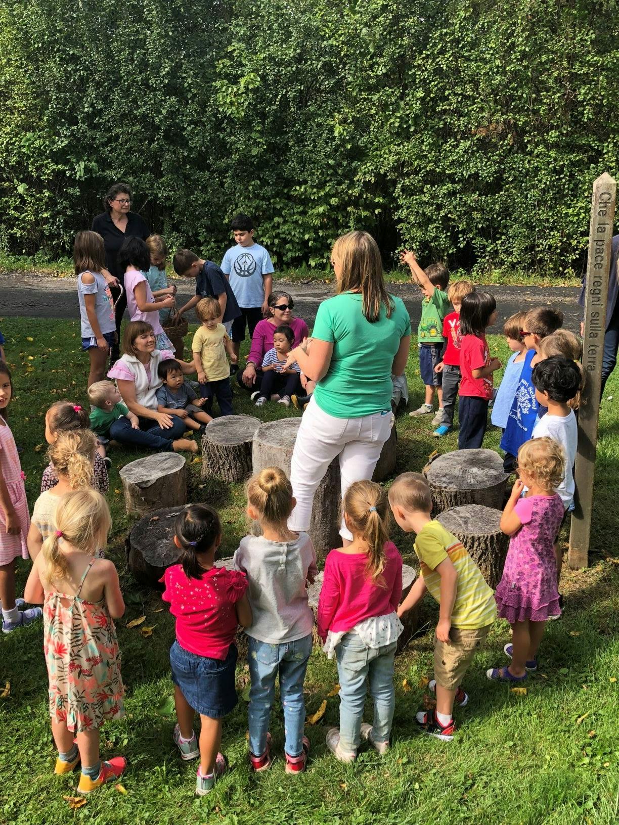 Adults and children gathered outdoors around tree stumps