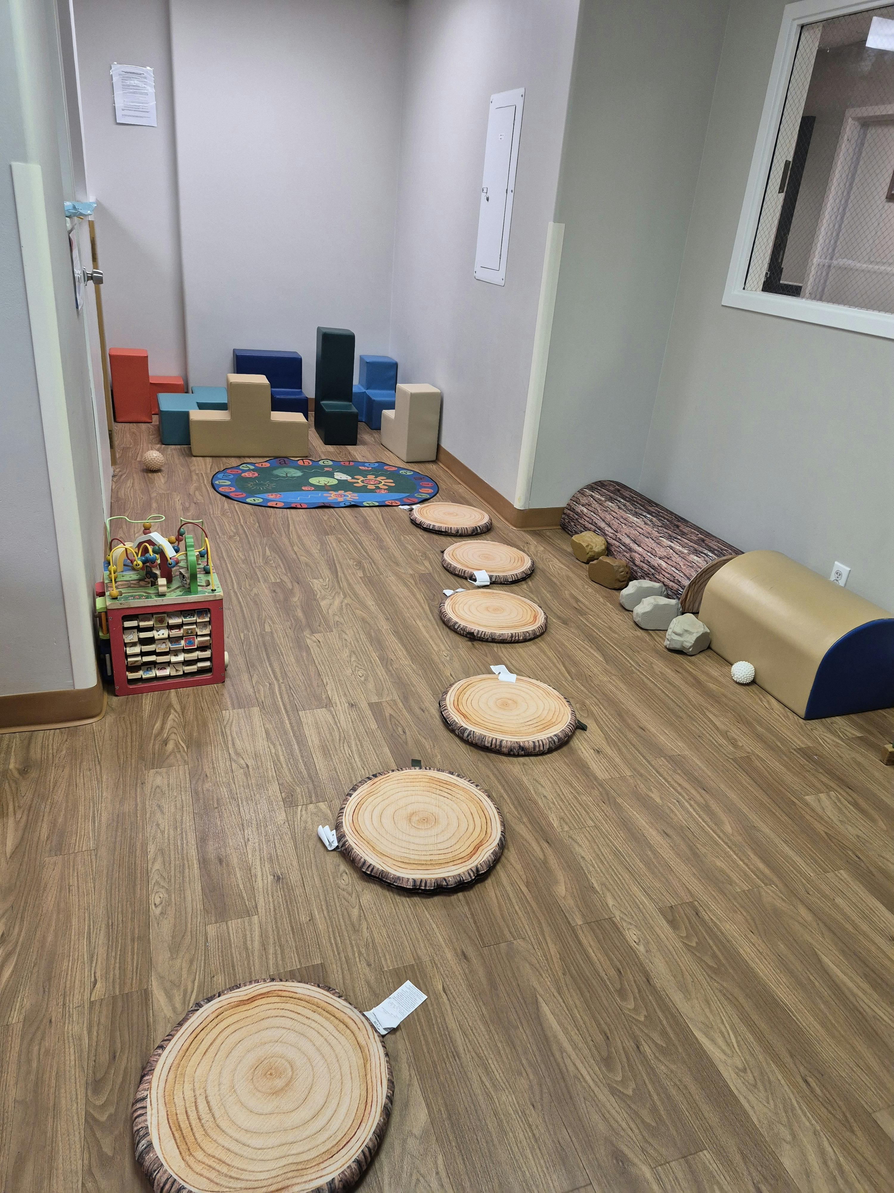 Playroom with soft block seating, a colorful rug, wooden step pads, and a log toy