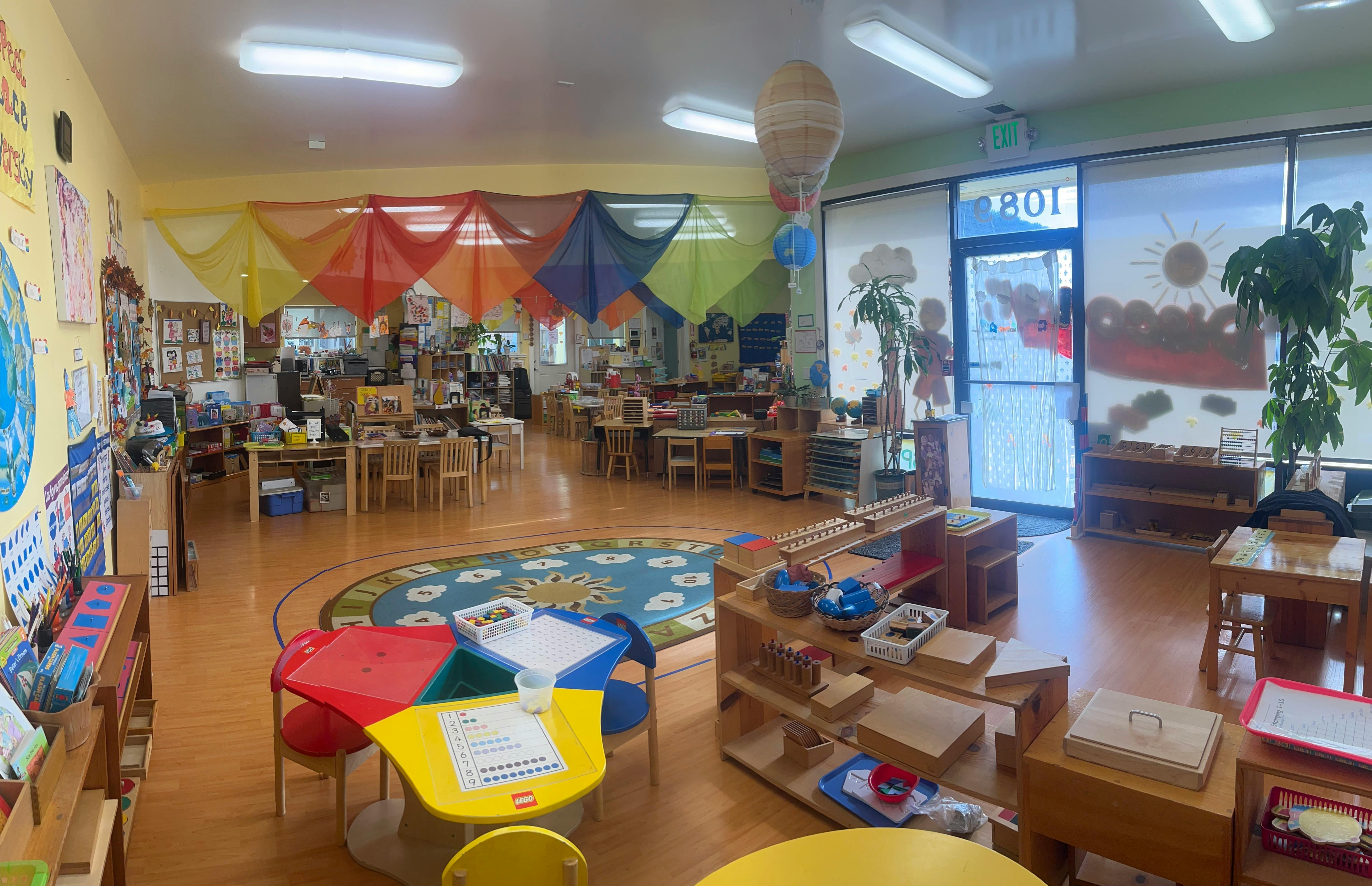 Empty classroom with small tables and chairs, shelves with learning materials