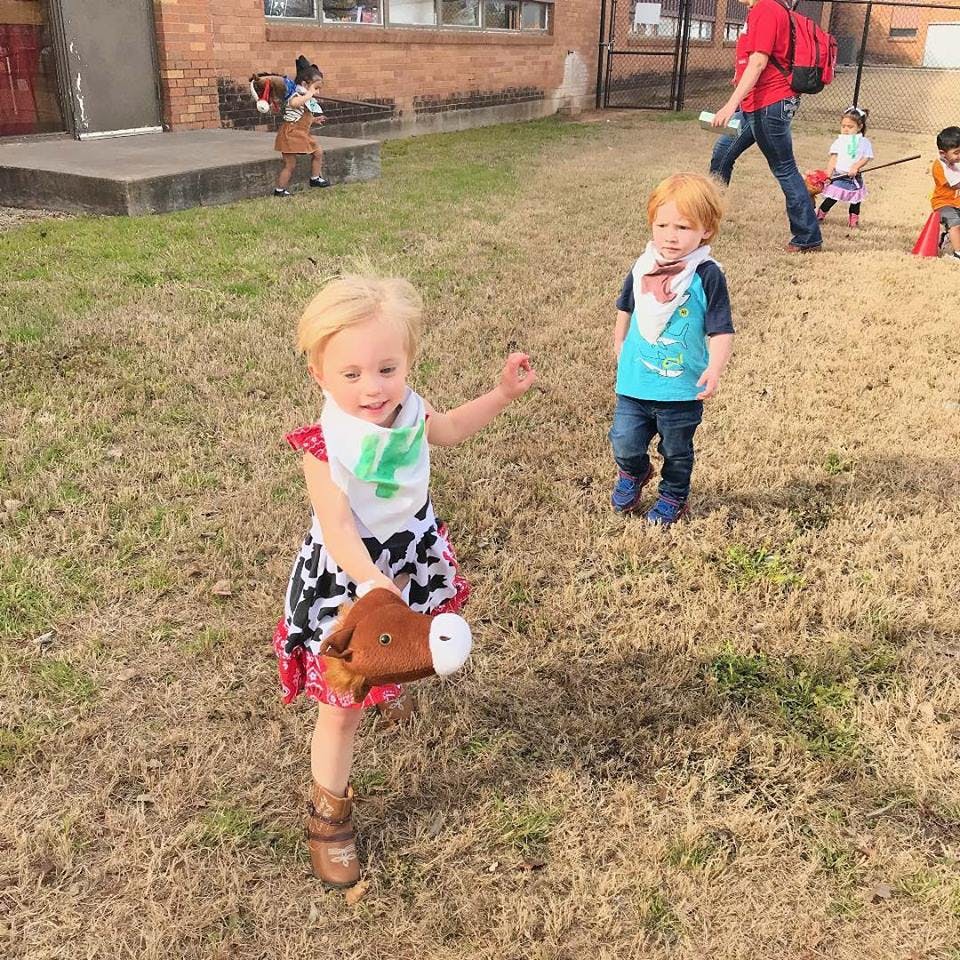 Child in a dress holding a toy horse, another child standing nearby