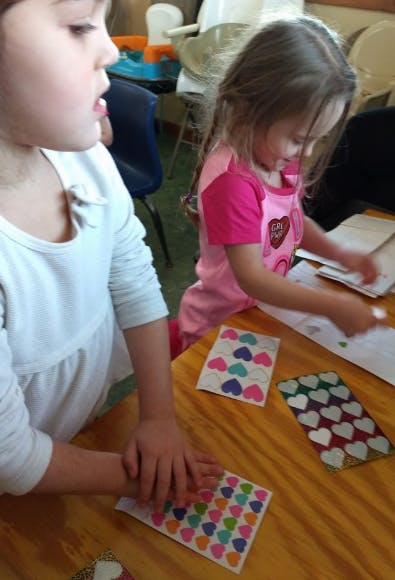 Two children working with heart stickers at a table