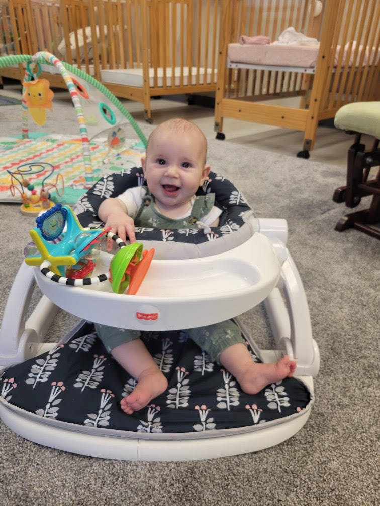 Child in a baby activity seat with toys