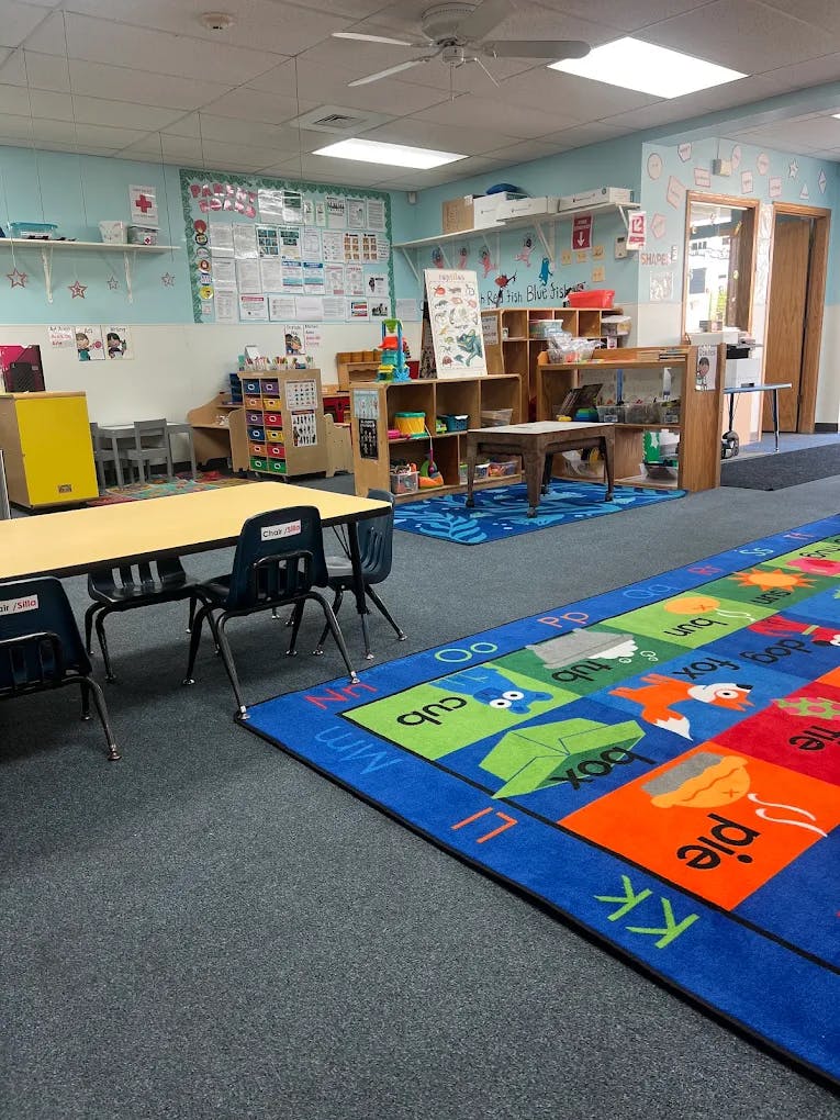 Classroom interior with small tables, chairs, and an alphabet rug