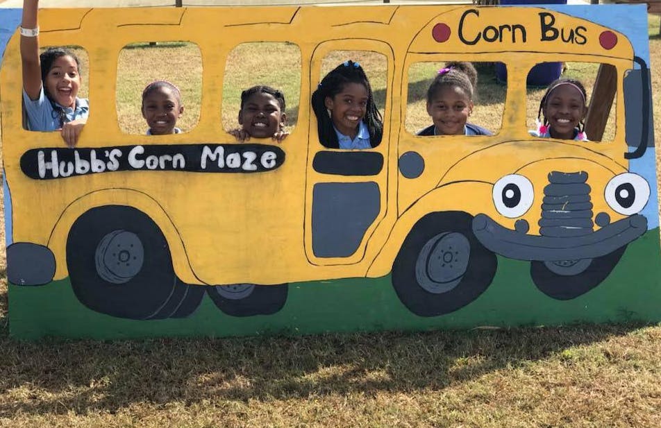 Children posing in a yellow bus cutout with "Hubb's Corn Maze" text
