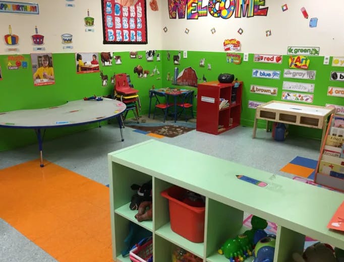 Classroom with green walls, tables, chairs, and storage shelves