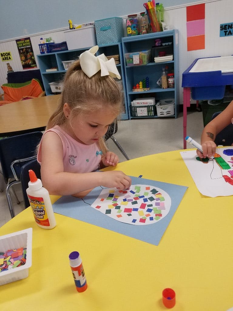 Child creating a collage with colorful paper squares in a classroom