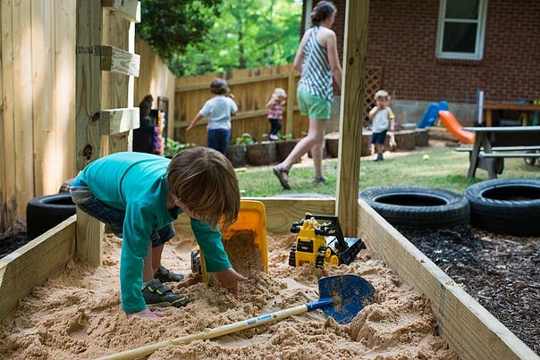 Child playing in a sandbox with a shovel and toy truck