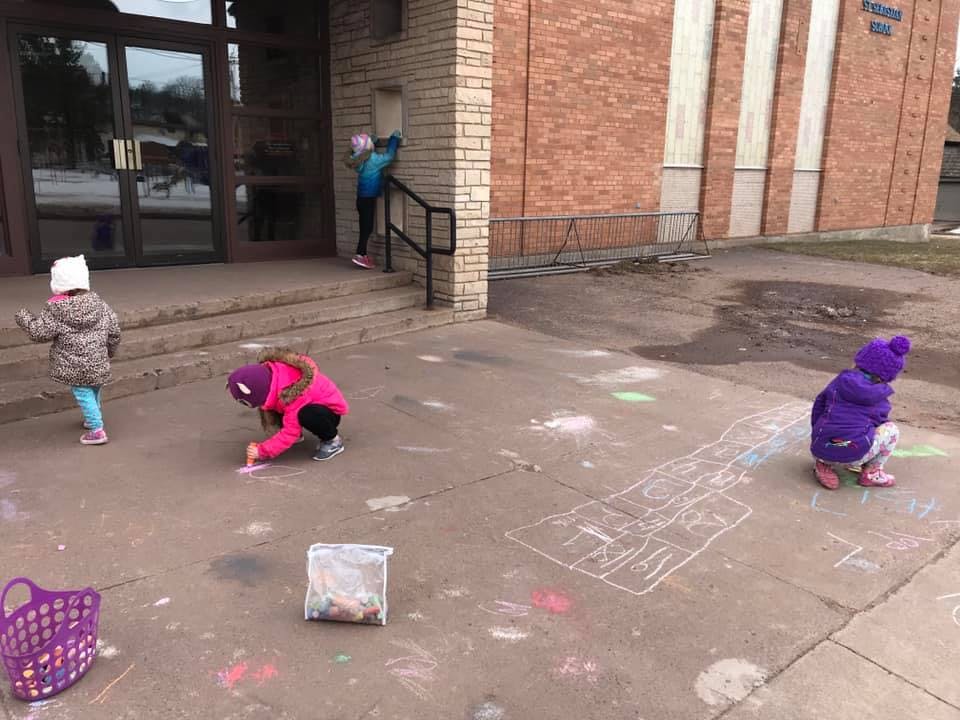 Children drawing with chalk on pavement outside pavement