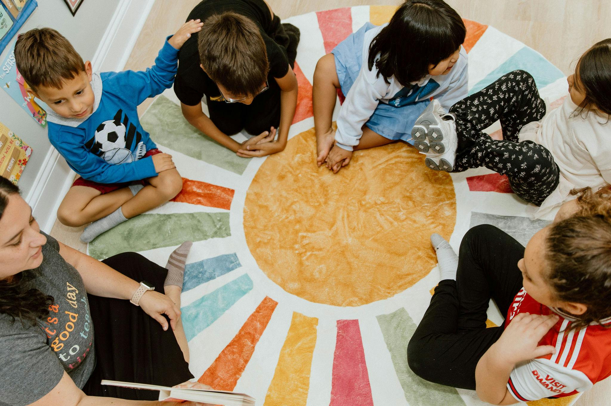 Adult reading a book to four children on a colorful sun rug