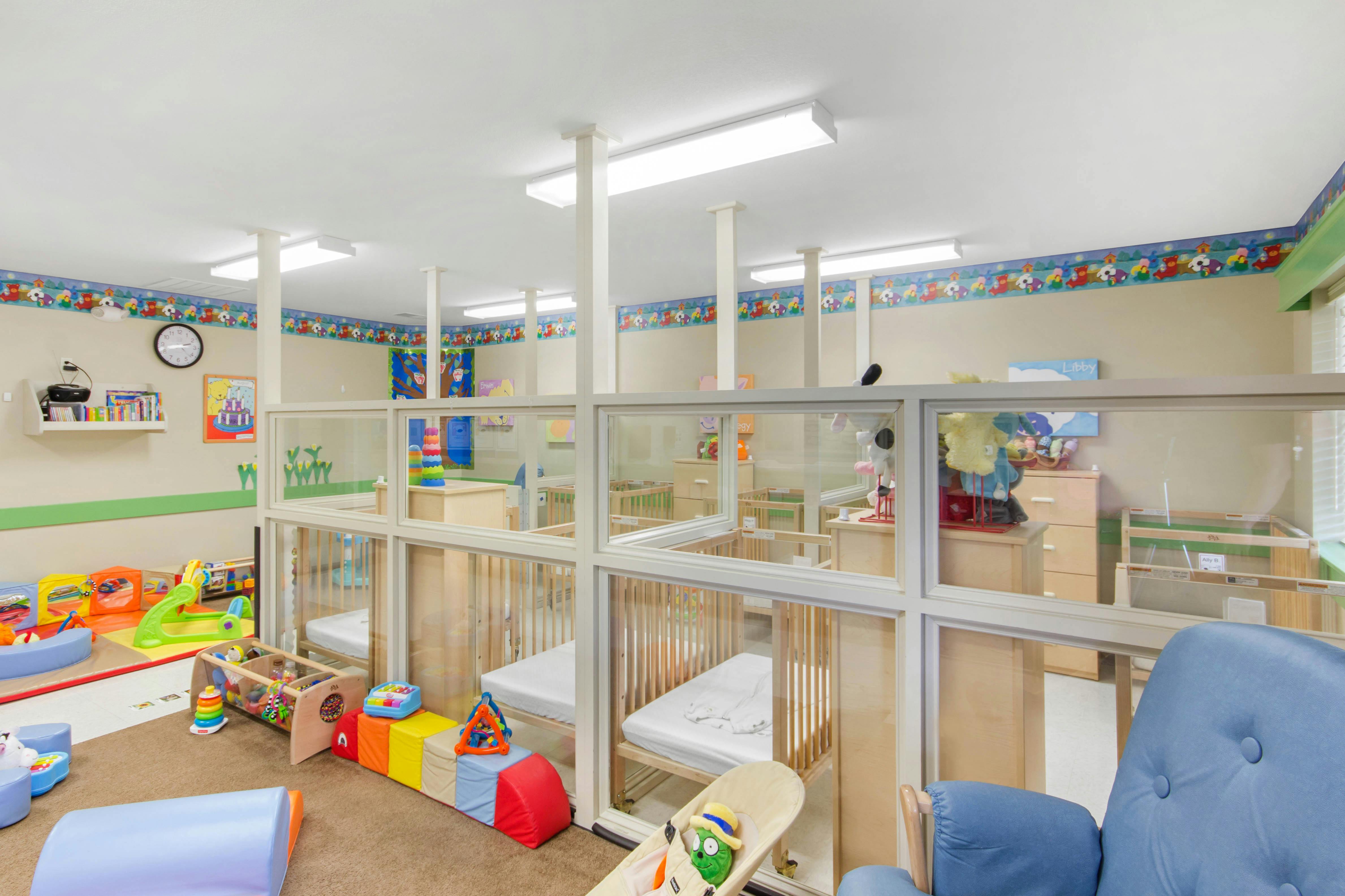 cribs in a daycare room with toys and a blue glider chair
