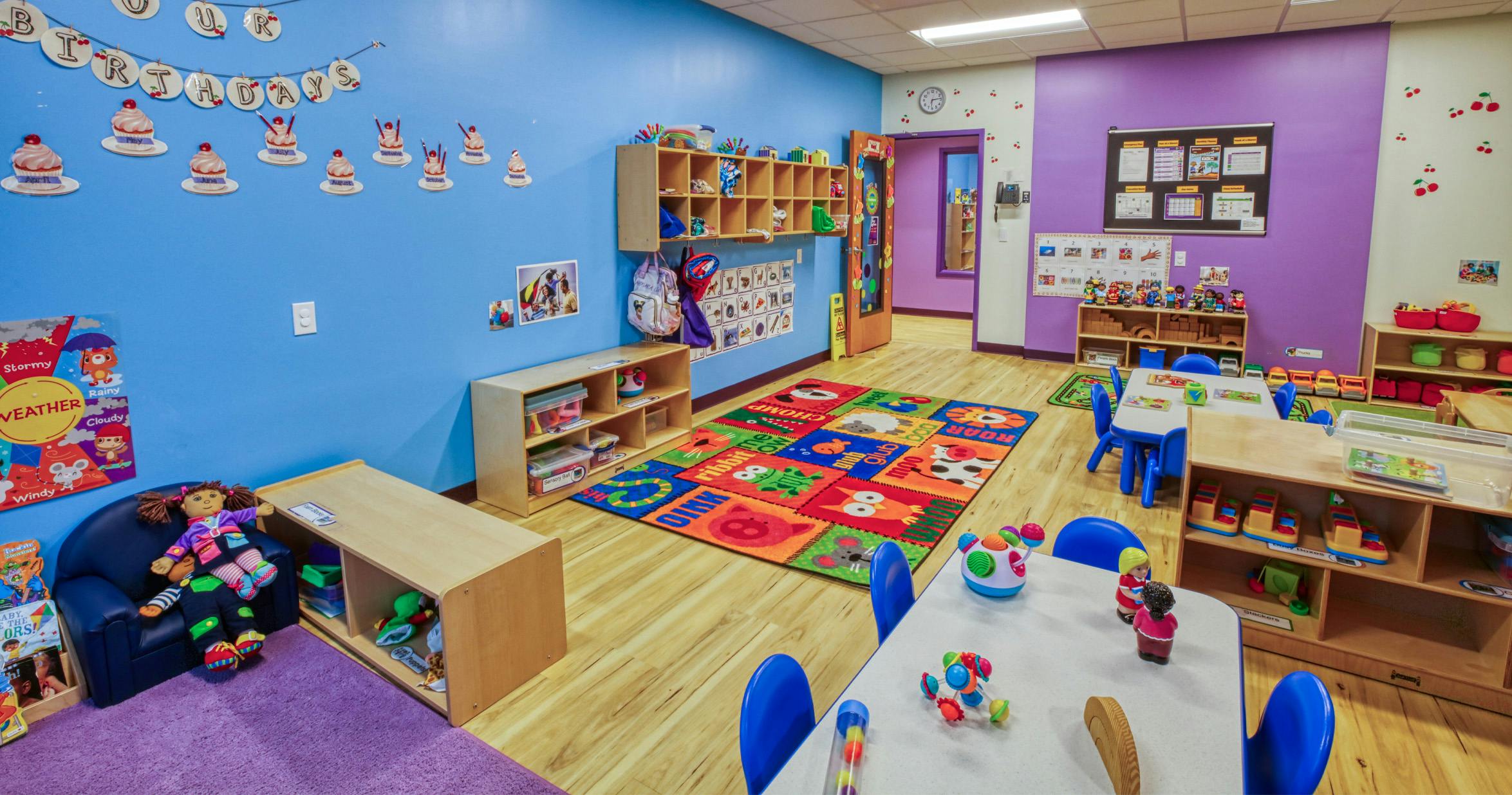 Colorful classroom with play rug, small tables and chairs, and various toys