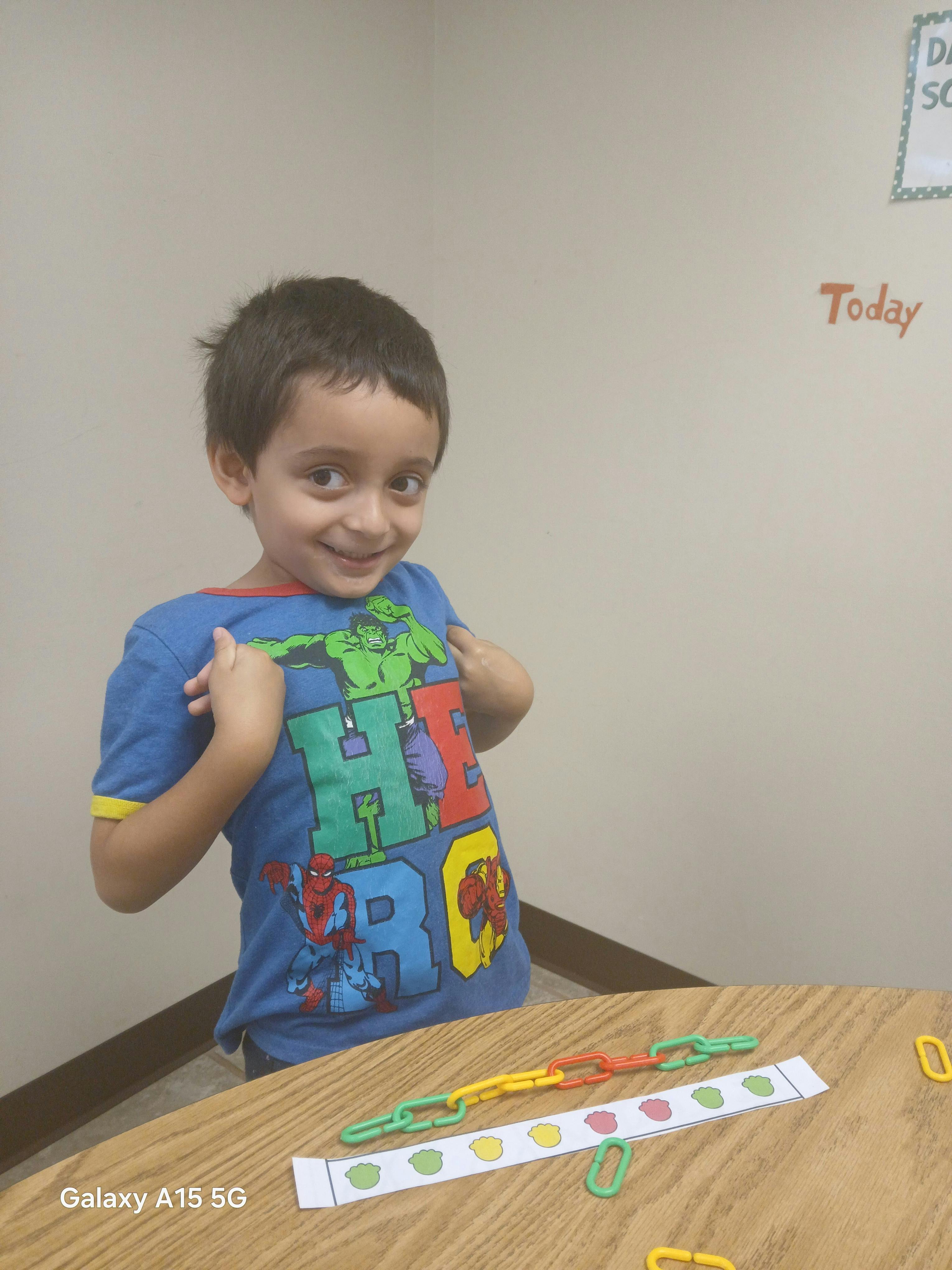 Child in a superhero shirt with colorful plastic links and a paper strip on a table