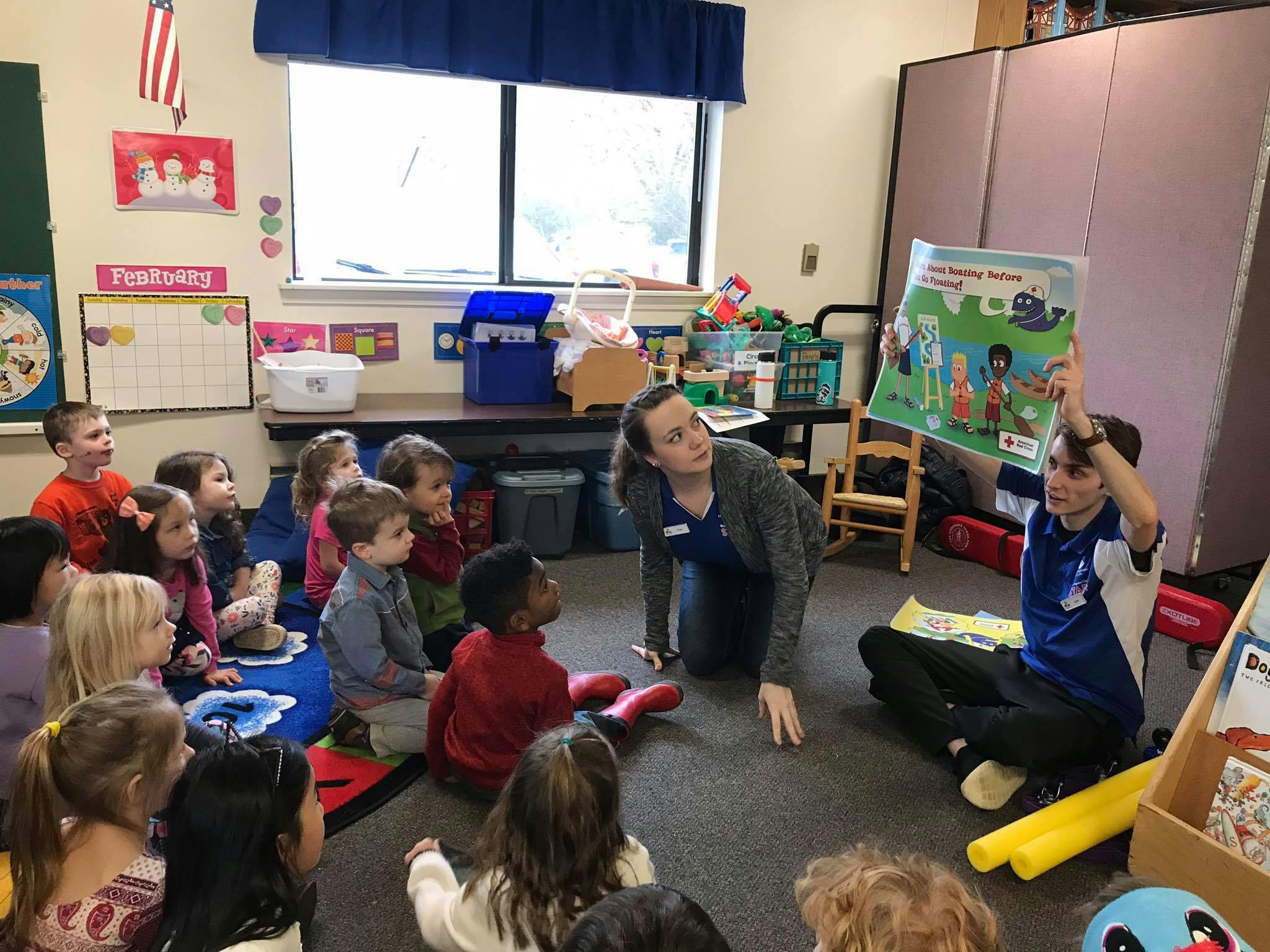 Two adults reading a book to a group of children in a classroom