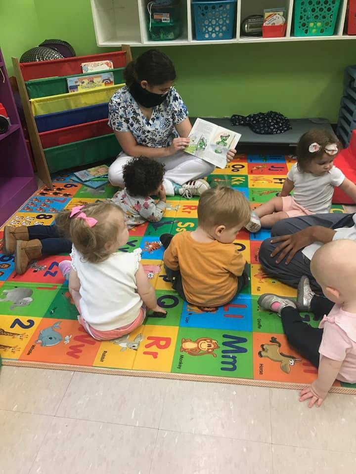 Person reading a book to multiple children on a colorful mat