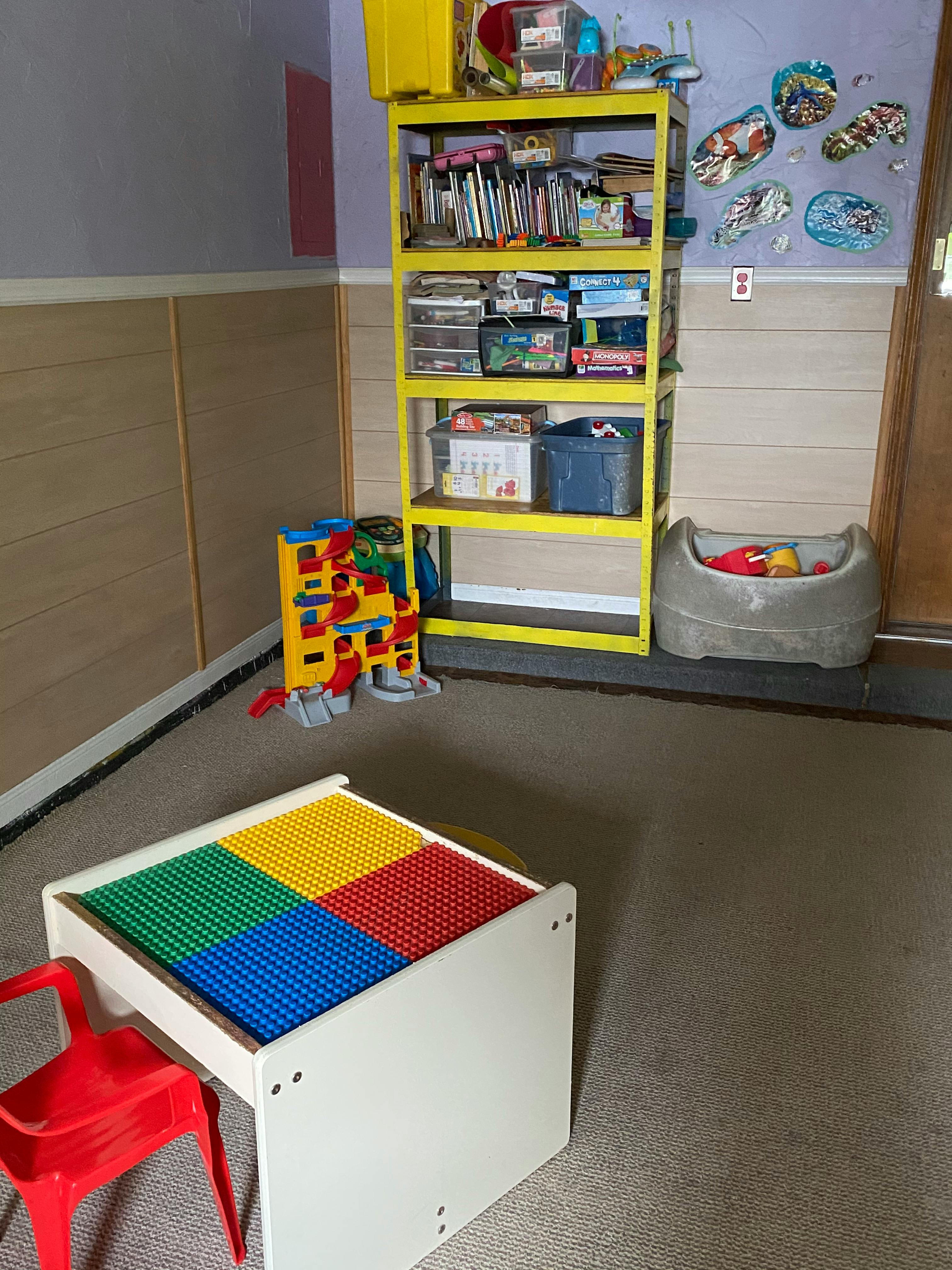 Playroom with a yellow shelf, toy bin, and a table with colorful building block surfaces