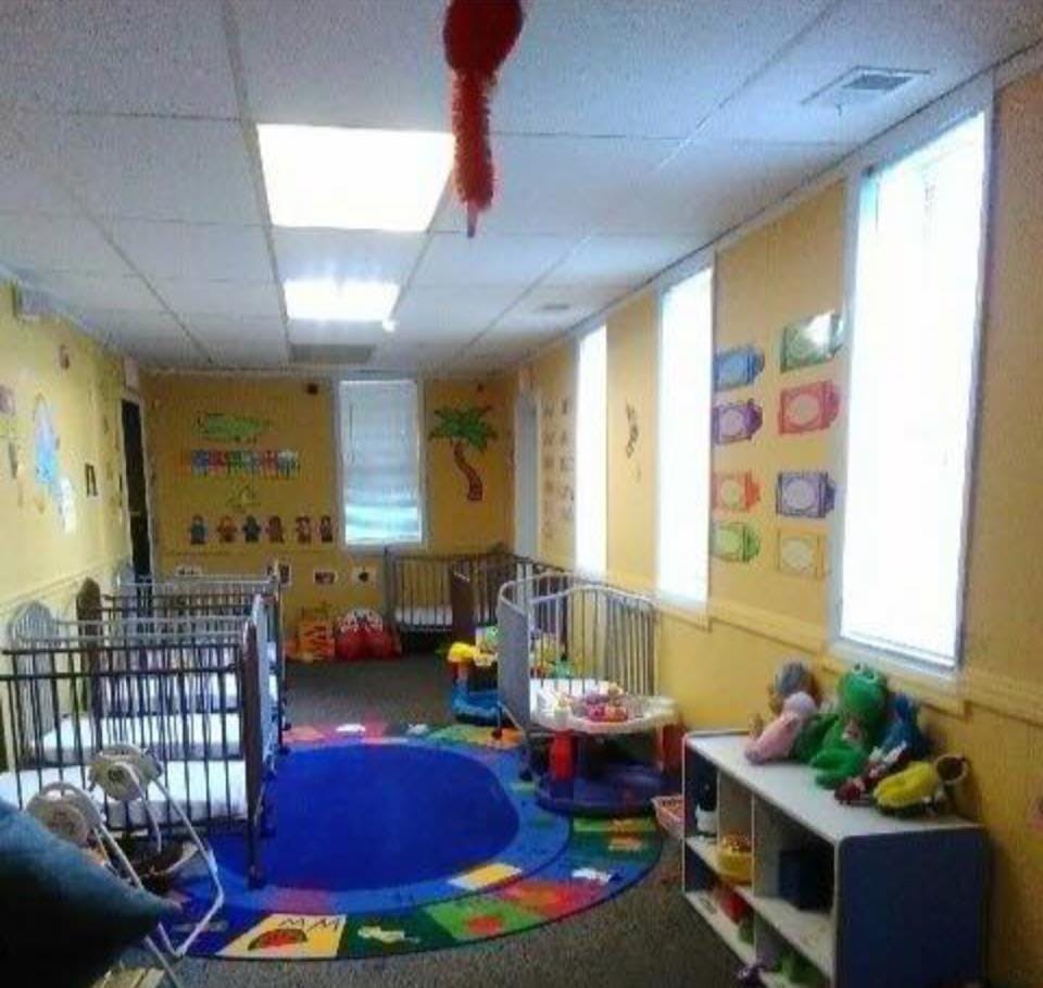 Daycare room with multiple cribs, colorful rug, and toys