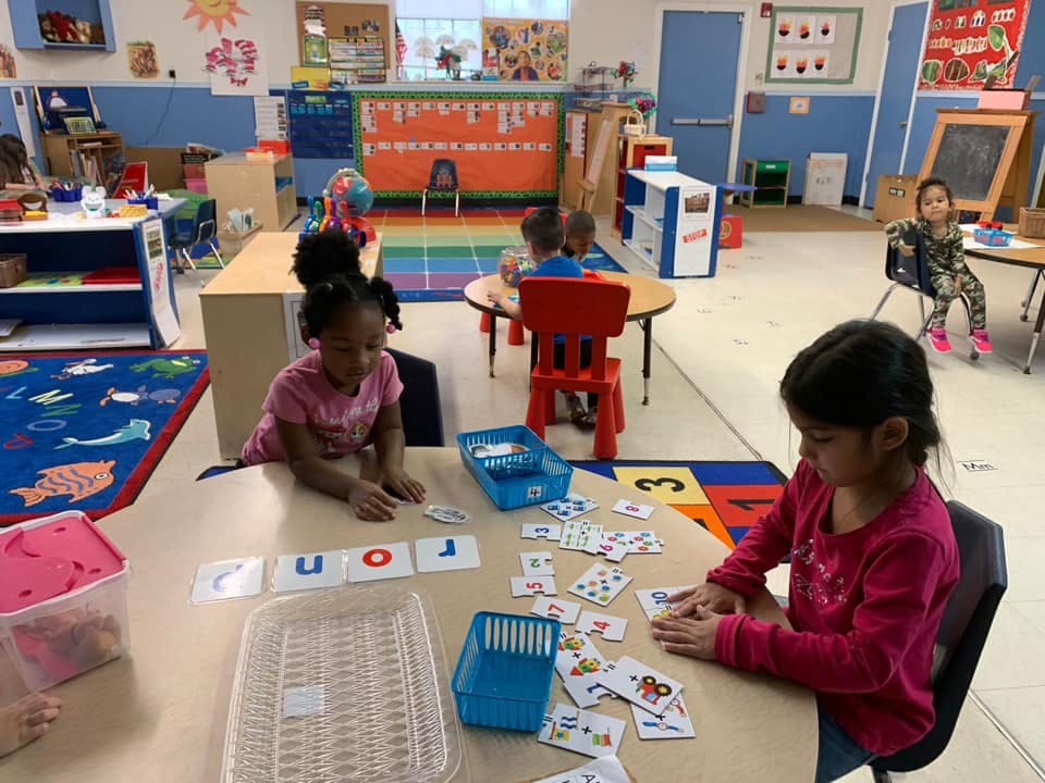 Children playing with cards and letter tiles at tables in a classroom
