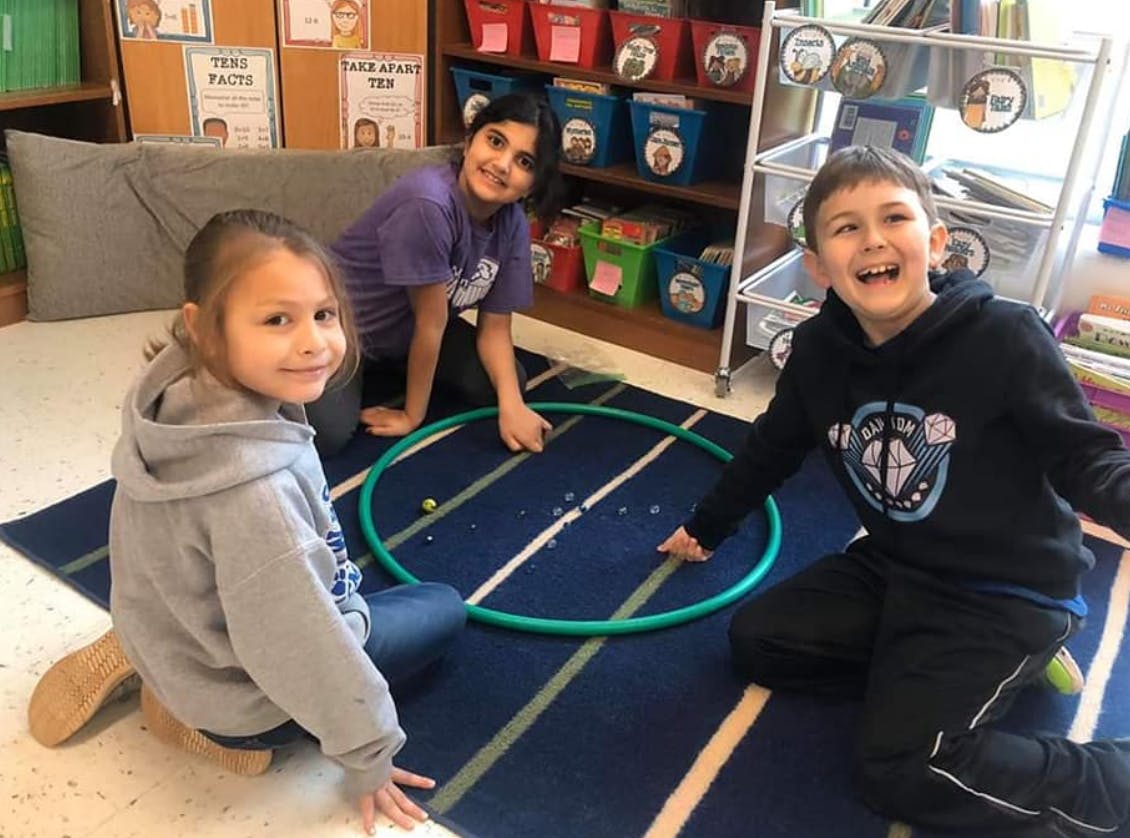 Three children playing with a hoop on a rug in a classroom