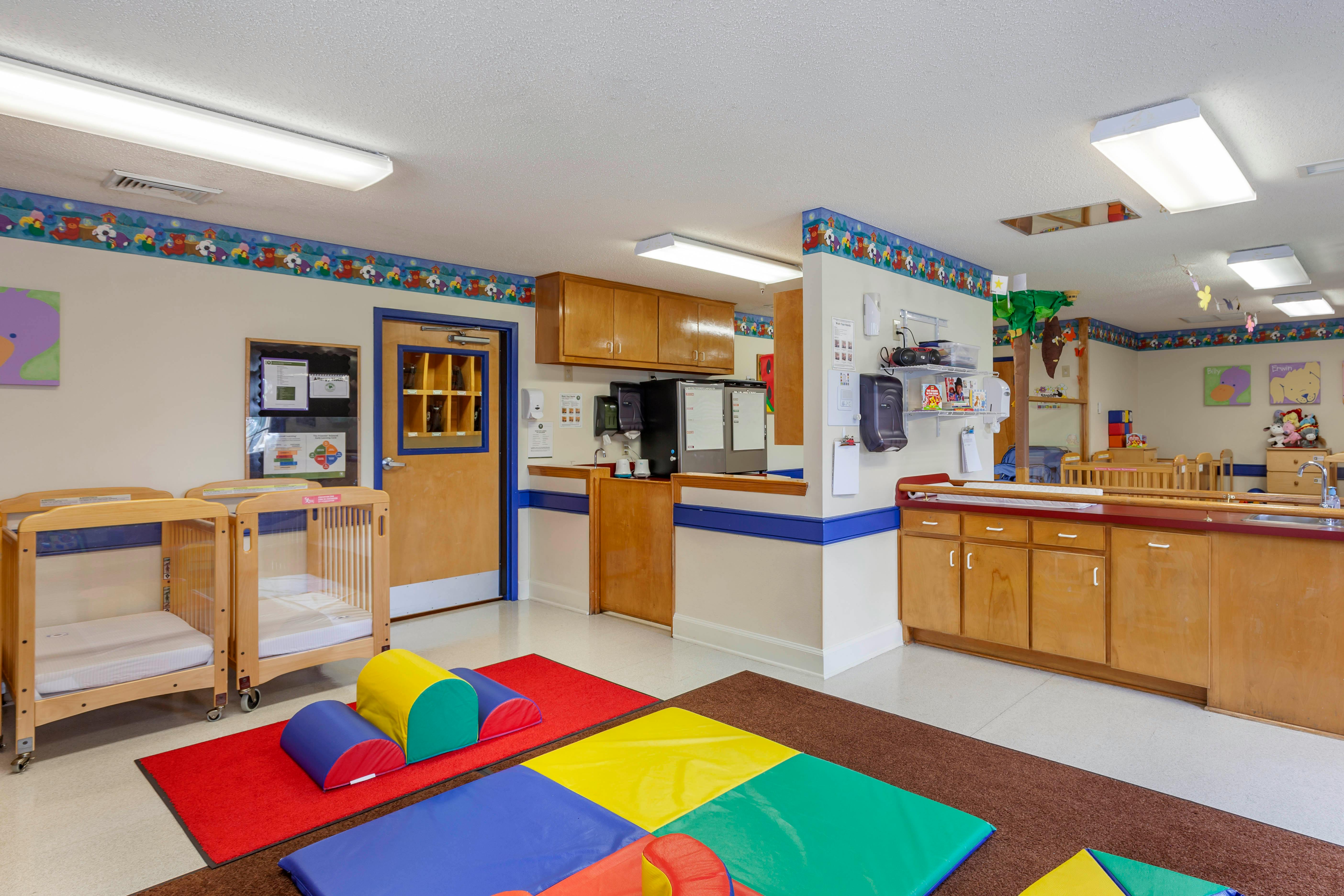 Room with two cribs, play mats, and a counter with cabinets