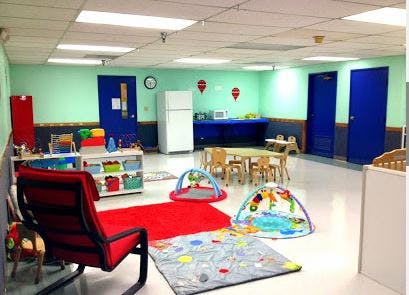 A brightly lit room with play mats, small tables and chairs, and storage shelves