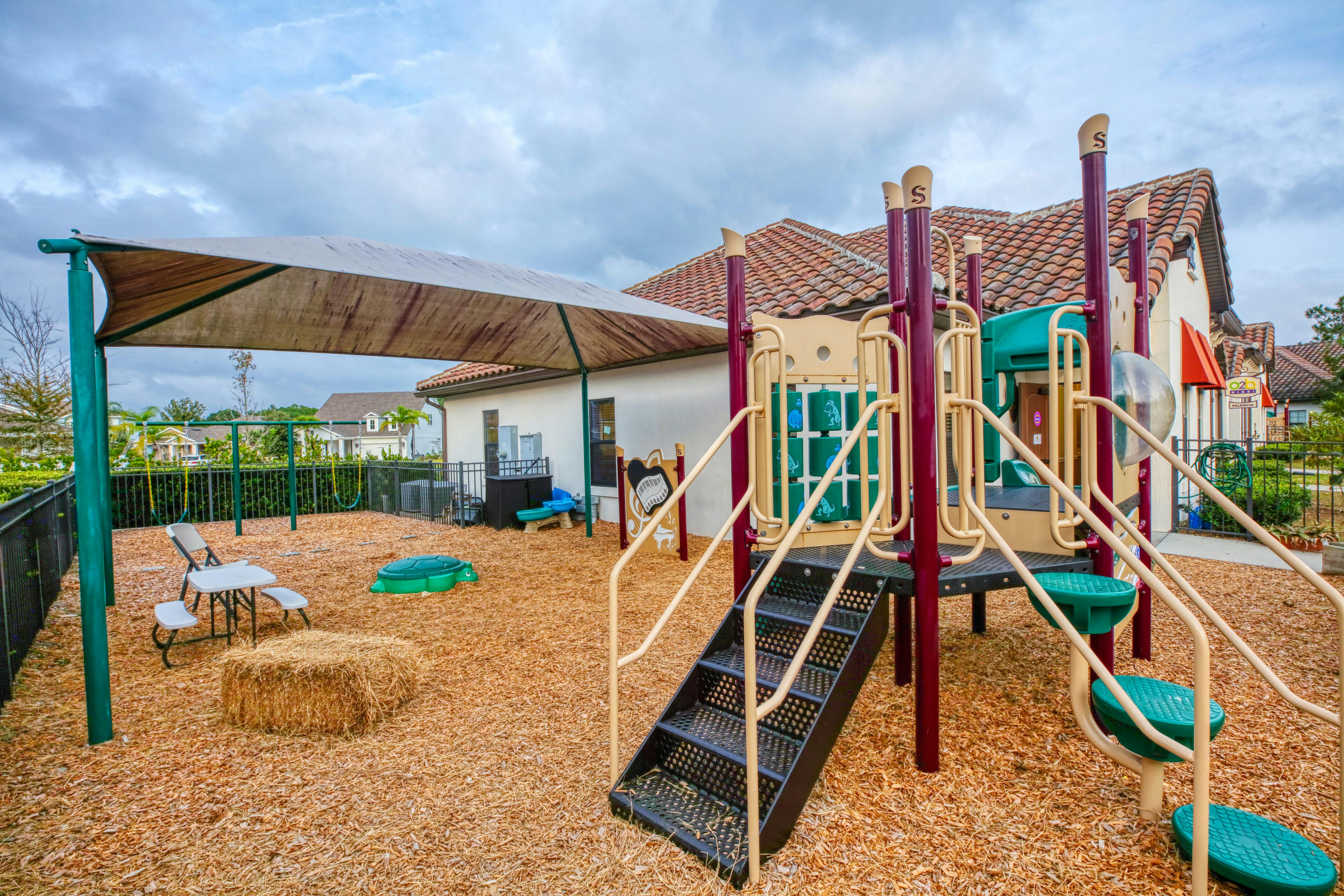 Empty playground with a slide, swings, and shade structure on wood chips