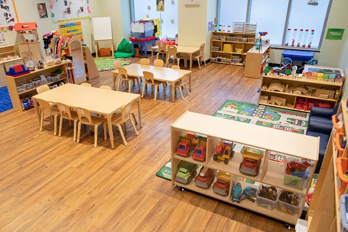 Classroom with child-sized tables and chairs, shelves with toys, and a rug