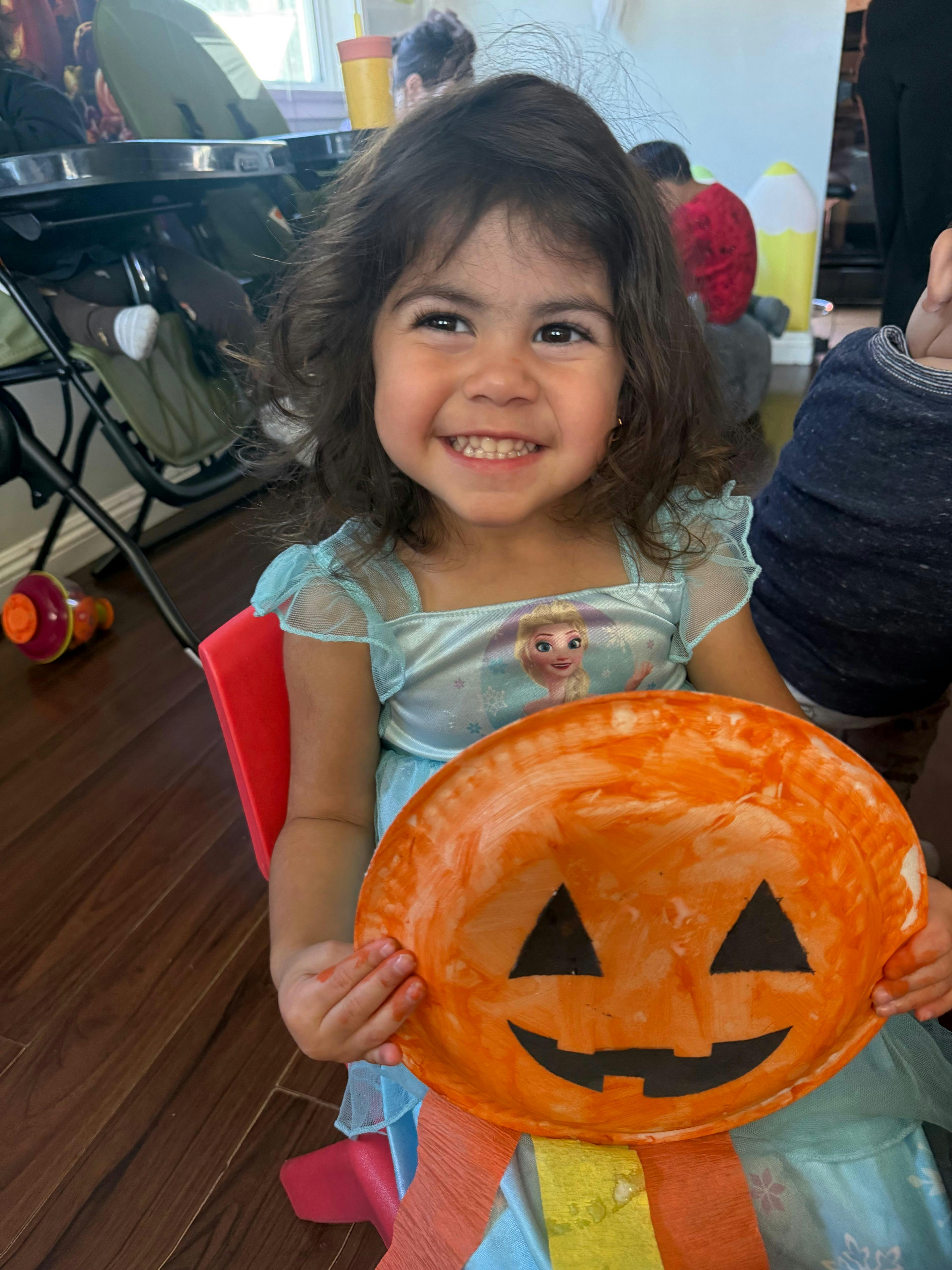 Child holding a homemade orange paper plate jack-o-lantern