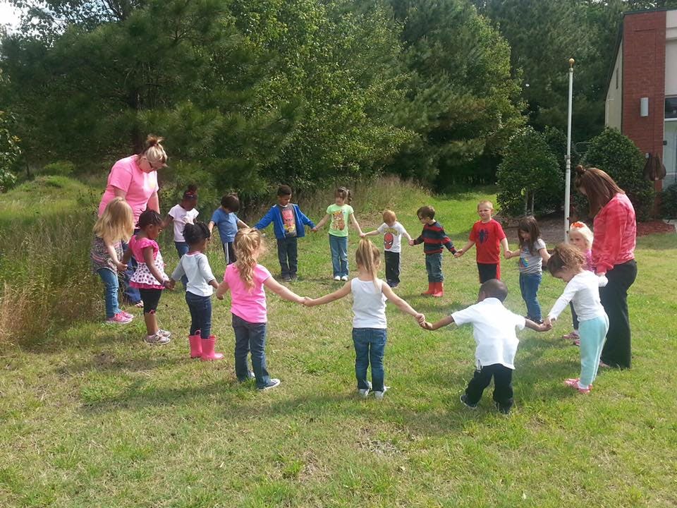Children and adults holding hands in a circle outdoors
