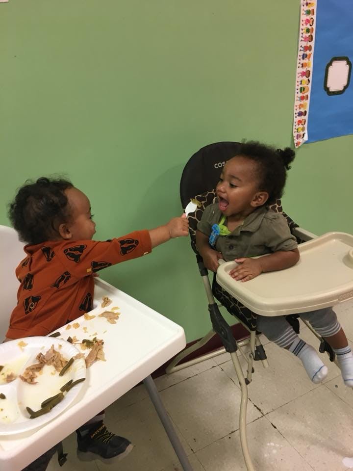 Child in high chair feeding another child in a high chair