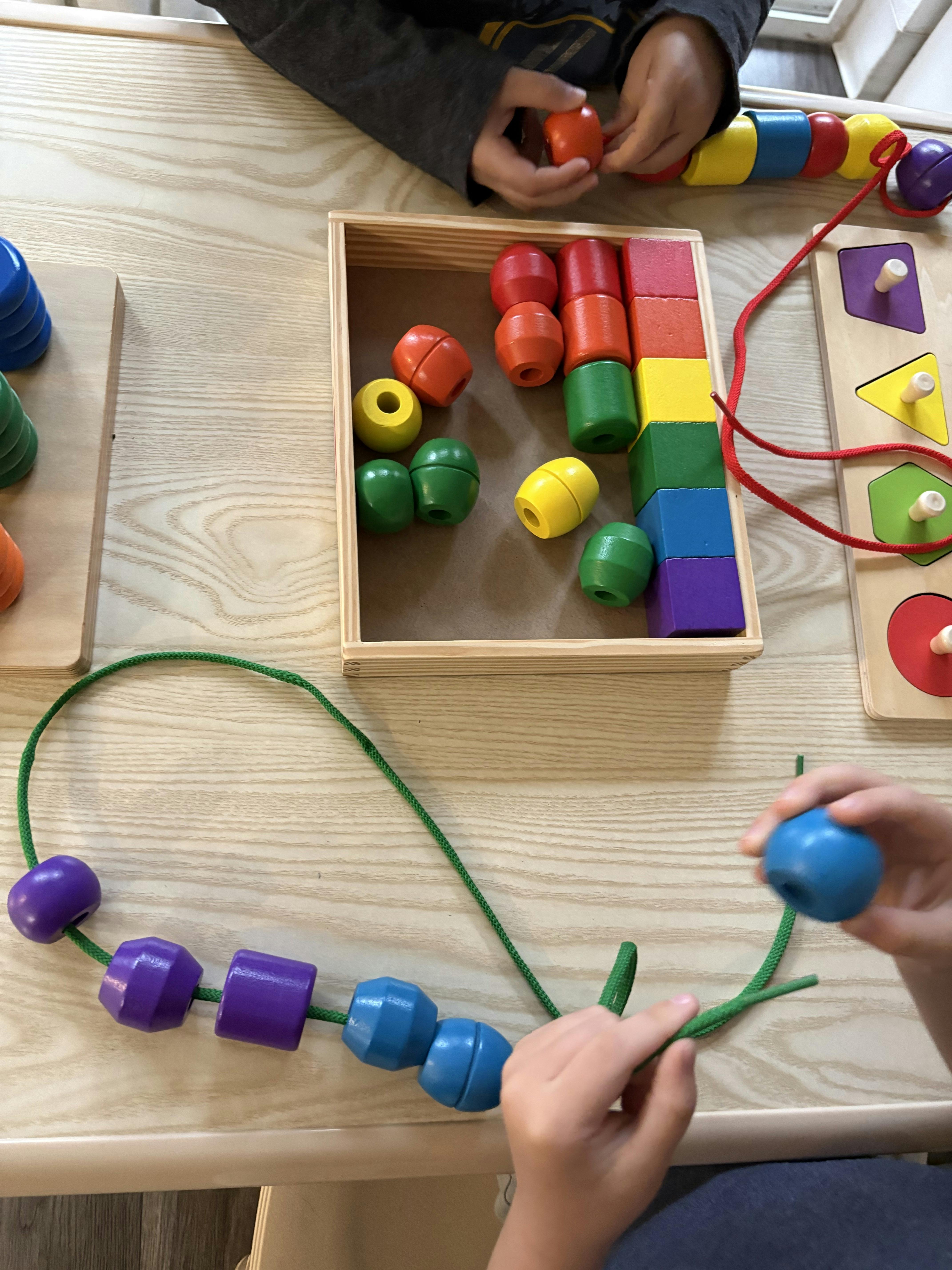 Child's hands playing with colorful lacing beads and blocks on a wooden table