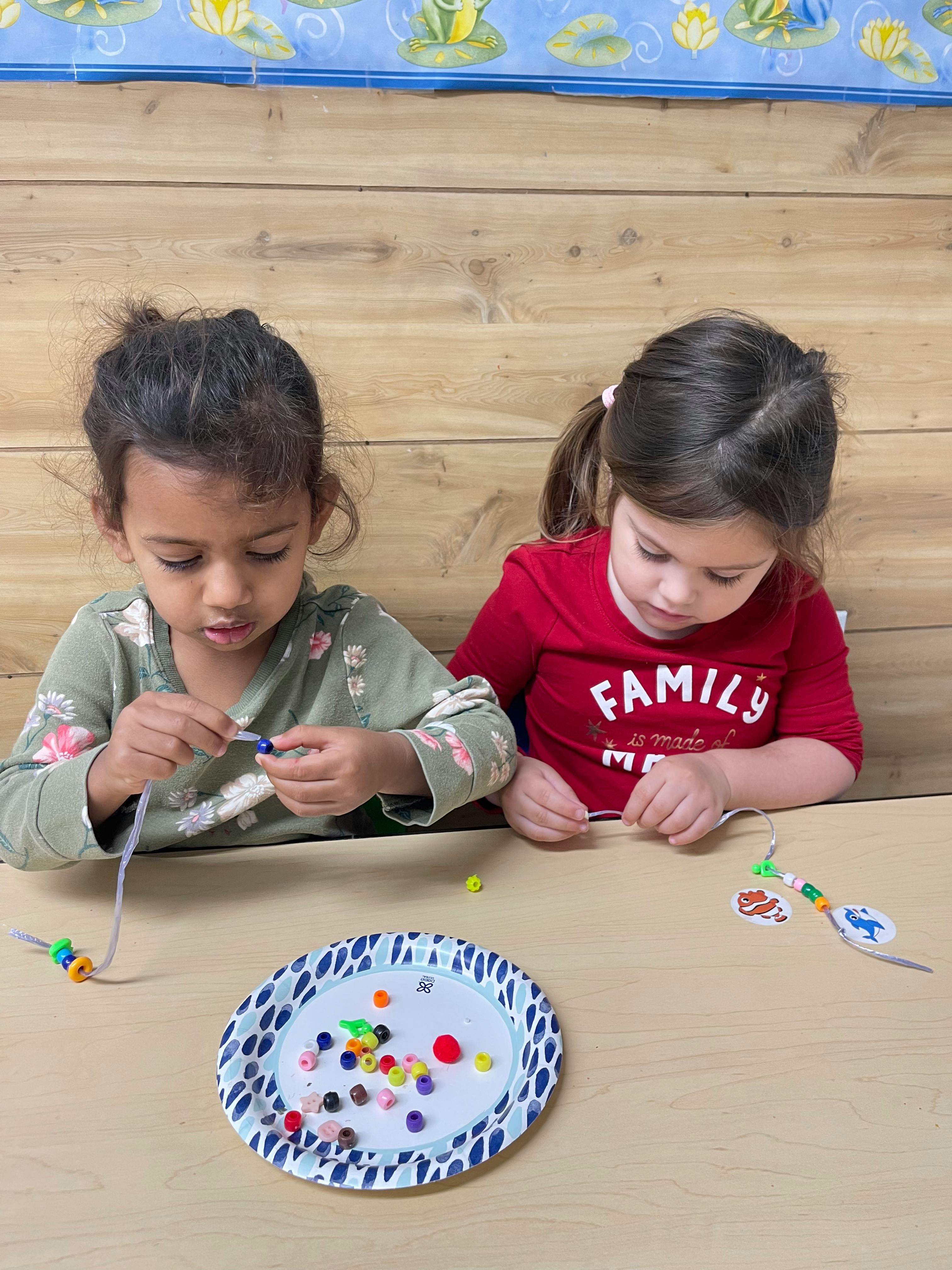 Two children stringing beads at a table