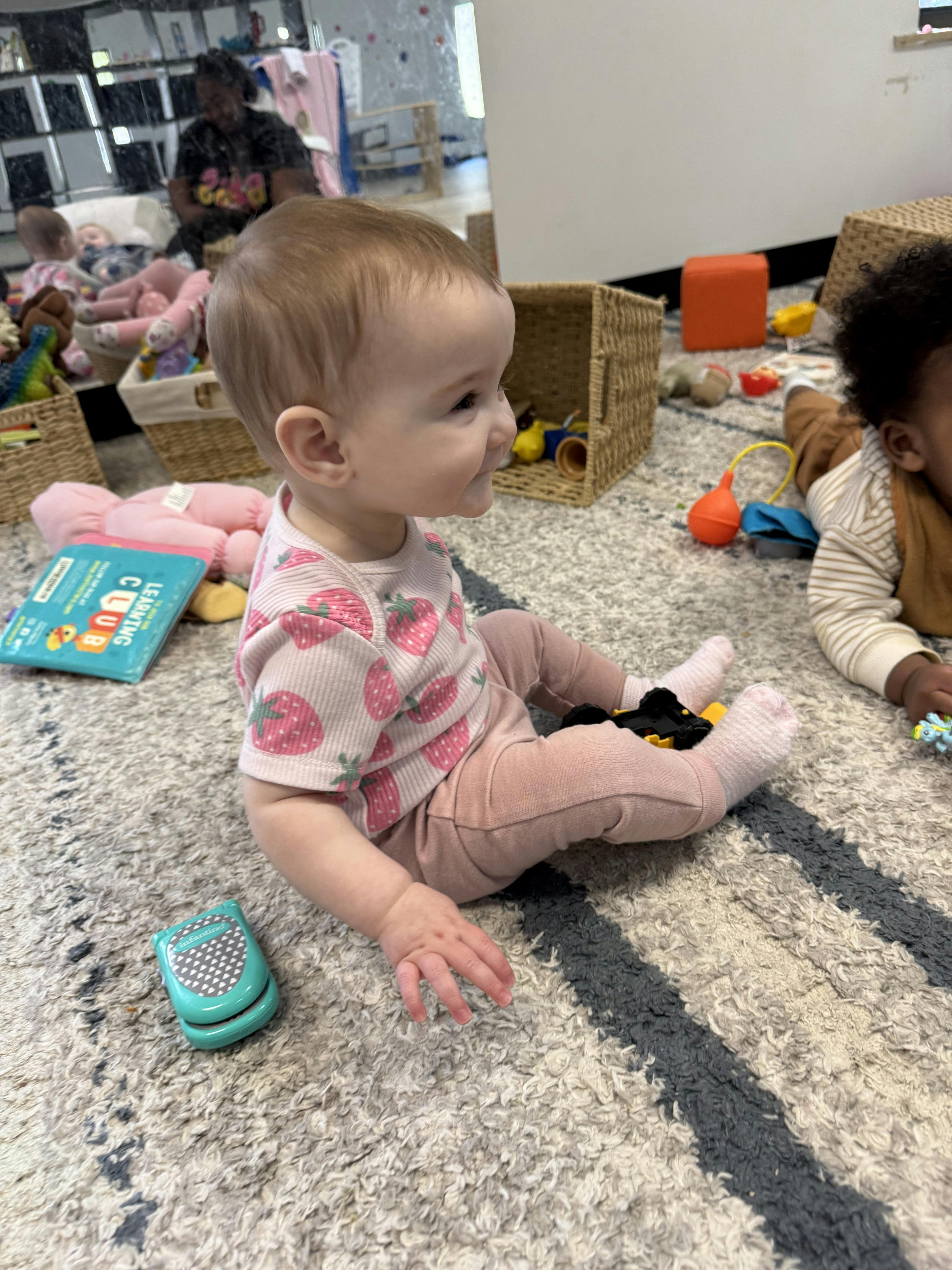 Child sitting on a rug with toys, looking to the side