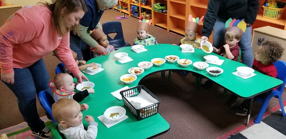 Adults helping children at a green table with bowls of food