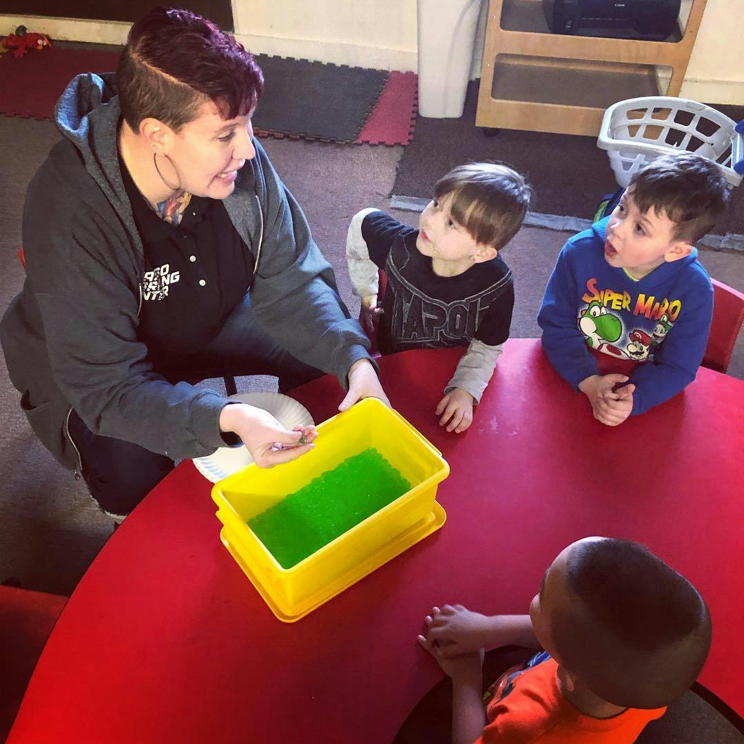 Person showing children a yellow container with green liquid