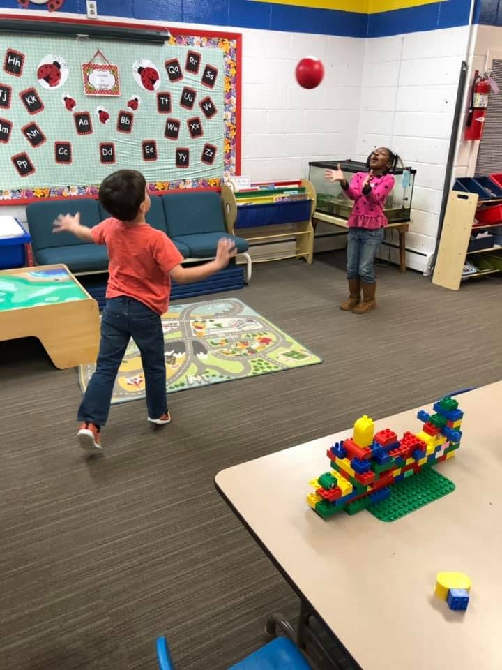 Child throwing a red ball to another child in a classroom