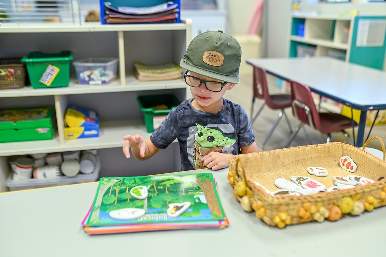 Child in a hat and glasses playing with a book and basket of cutouts