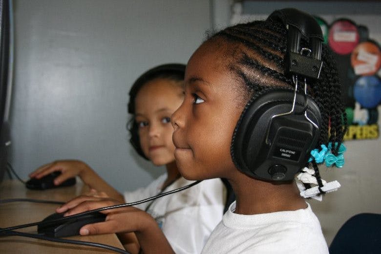 Two children wearing headphones and using computer mice