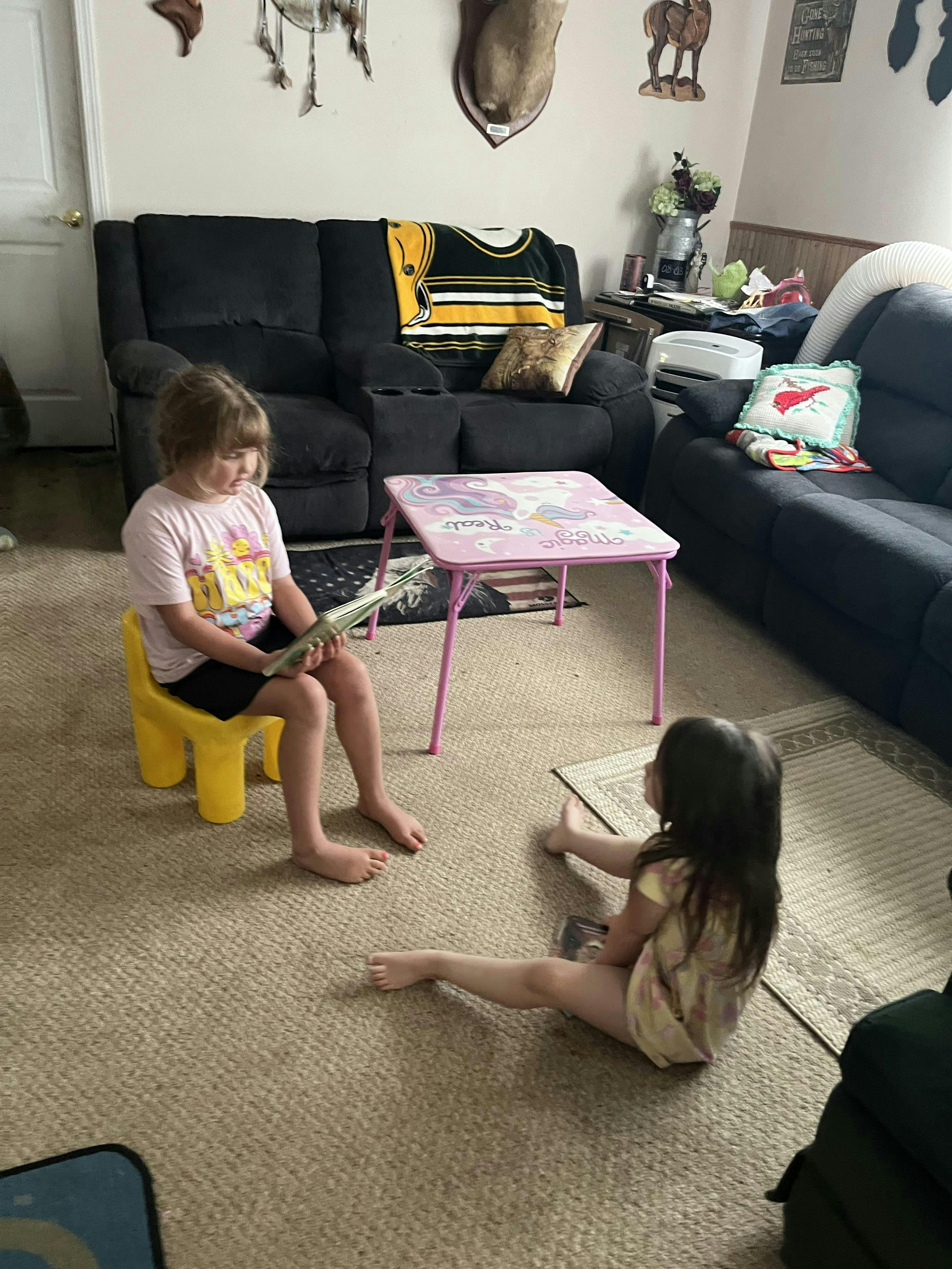 Child sitting on yellow chair reading a book, another child sitting on the floor