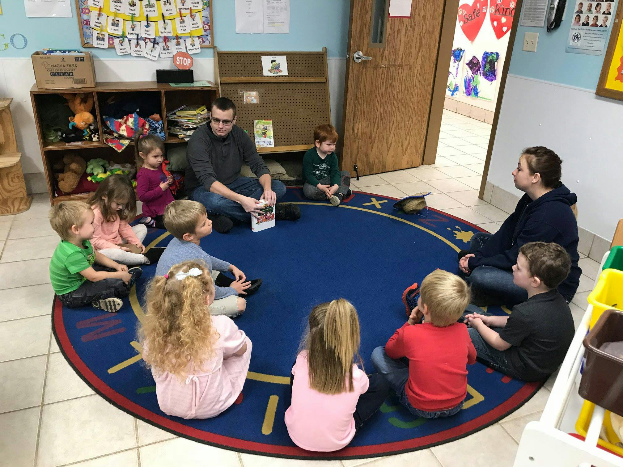 Adults and children sitting in a circle on a rug in a classroom
