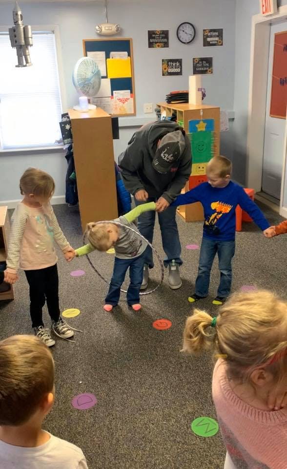 Adult and children playing with a hula hoop in a classroom